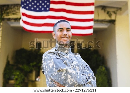 Portrait of happy biracial male american soldier wearing military uniform standing outside the house. American flag, patriotism and military service.