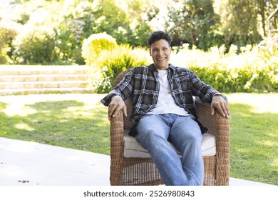 Portrait of happy biracial man sitting in chair in sunny garden, copy space. Outdoors, expression, leisure and nature unaltered. - Powered by Shutterstock