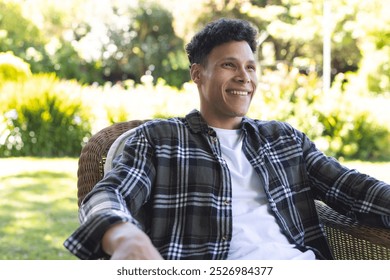 Portrait of happy biracial man sitting in chair in sunny garden, copy space. Outdoors, expression, leisure and nature unaltered. - Powered by Shutterstock