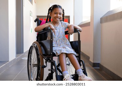 Portrait of happy biracial schoolgirl sitting in wheelchair at elementary school corridor. Disability, education, childhood, development, learning and school, unaltered. - Powered by Shutterstock