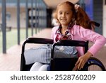 Portrait of happy biracial schoolgirl in wheelchair, smiling in school corridor. Education, childhood, elementary school, inclusivity and learning concept.