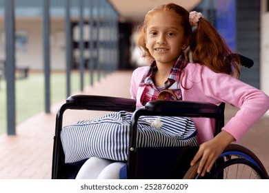 Portrait of happy biracial schoolgirl in wheelchair, smiling in school corridor. Education, childhood, elementary school, inclusivity and learning concept. - Powered by Shutterstock