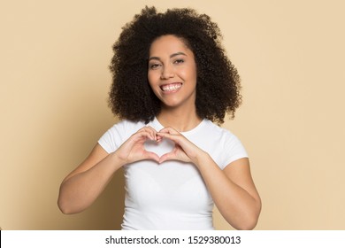 Portrait of happy biracial young woman in white t-shirt isolated on brown studio background look at camera show heart, smiling african American millennial girl make gesture sending virtual love hugs - Shutterstock ID 1529380013
