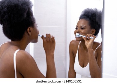 Portrait Happy Black African American Girl Brushing Teeth In The Bathroom. Morning Routine With Toothbrushes Woman Looking In Mirror