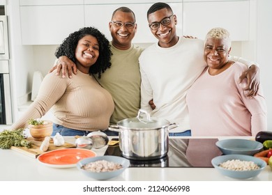 Portrait of happy black family cooking vegan food inside kitchen at home - Main focus on mother face
