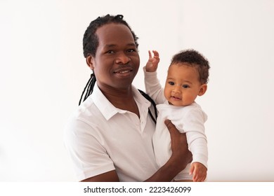 Portrait Of Happy Black Father With Cute Little Baby On Hands Standing Near Window At Home, African American Man Holding His Adorable Infant Son And Smiling At Camera, Enjoying Fatherhood, Copy Space