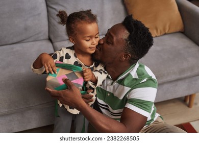 Portrait of happy Black father presenting gift to cute little daughter at home and kissing her on cheek - Powered by Shutterstock