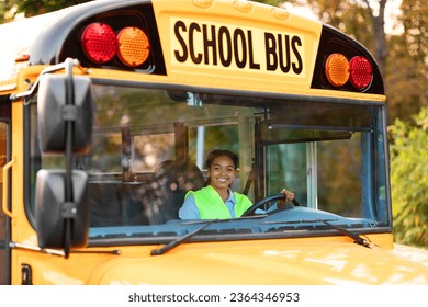 Portrait Of Happy Black Female Driver Driving Yellow School Bus, Beautiful Young African American Lady In Reflecting Vest Looking Through Window, Holding Steering Wheel An Smiling At Camera