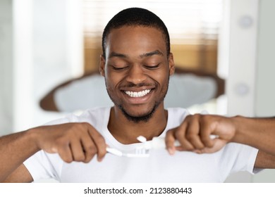 Portrait Of Happy Black Guy Squeezing Toothpaste On Toothbrush In Bathroom, Handsome Young African American Man Preparing For Brushing Teeth, Making Daily Dental Hygiene At Home, Closeup Shot