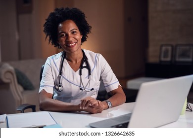 Portrait of happy black healthcare worker sitting at desk in doctor's office and looking at camera. 