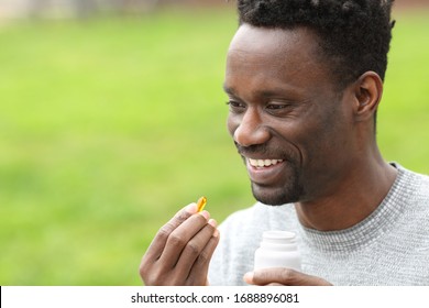 Portrait Of A Happy Black Man Taking Vitamin Omega3 Pill In The Park