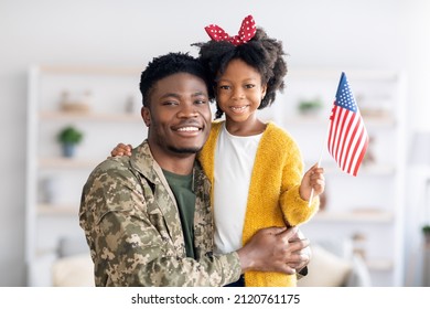 Portrait Of Happy Black Military Dad And His Daughter With American Flag In Hand Posing At Home, Cheerful Soldier Father In Camo Uniform And Cute Female Child Smiling At Camera, Copy Space