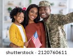 Portrait Of Happy Black Military Man Taking Selfie With Wife And Little Daughter At Home, Happy Family Celebrating Reunion And Smiling At Camera, Cute Girl Holding American Flag, Closeup