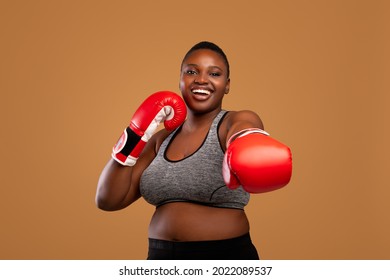 Portrait Of Happy Black Millennial Woman In Sportswear Wearing Red Boxing Gloves, Confident Young African American Lady Ready For Box Training, Posing Over Brown Background In Studio, Copy Sace - Powered by Shutterstock