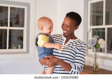 Portrait of happy black mother holding cute toddler laughing together at home. Cheerful african woman cuddling smiling little boy in hand and playing. Mature black nanny playing with little boy.