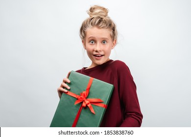 Portrait Of Happy Blonde Girl 12-15 Years Old Dressed In Casual Sweater, Holding Gift Decorated With Ribbon. Studio Shot White Background, Isolated. New Year, Women's Day, Birthday, Holiday Concept