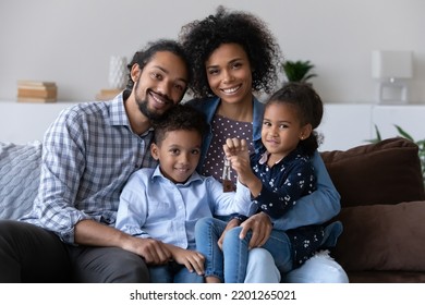 Portrait of happy bonding African American family showing keys to camera, sitting on couch, Joyful adorable small children and caring young multiracial couple parents celebrating moving into own home. - Powered by Shutterstock