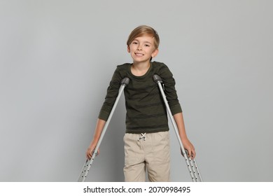 Portrait of happy boy with crutches on grey background