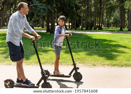 Portrait of happy boy in protective helmet having ride on motorized kick scooter with smiling father at park, spending time together with family on father's day outside, having fun, free copy space
