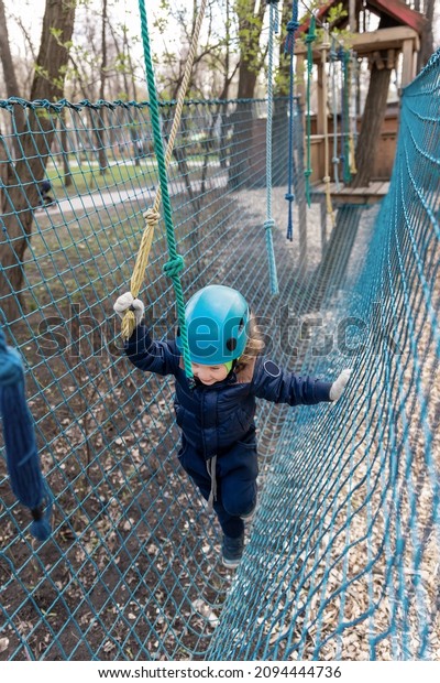 Portrait happy brave courage little toddler child\
boy wear safety equipment helmet enjoy passing obstacle course\
forest rope adventure park on cold winter day. Active outside\
leisure amusement camp