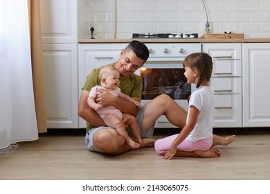 Portrait Of Happy Brunette Man Wearing Casual Style T Shirt Sitting On Floor In Kitchen With Kids, Father Holding Baby Ina Hands, Dad Spending Time With Kids During Day Off.