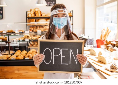 Portrait Of A Happy Business Owner With An Open Sign On The Bakery Shop And Smiling - Food And Drinks Concepts. Woman Working At A Bakery Wearing A Facemask To Avoid The Coronavirus