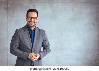 Portrait of happy businessman with arms crossed standing in office. Portrait of young happy businessman wearing grey suit and blue shirt standing in his office and smiling with arms crossed - Shutterstock ID 2278103089