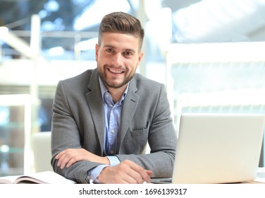 Portrait of happy businessman sitting at office desk, looking at camera, smiling.