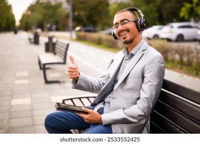 Portrait of happy businessman who is messaging on digital tablet. Man sitting on bench in the city and using digital tablet. - Powered by Shutterstock