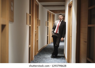 Portrait of happy businessman working in office, financial consultant smiling and looking at camera. The man is leaning on wall in office corridor, with happy and relaxed expression. - Shutterstock ID 1293798628