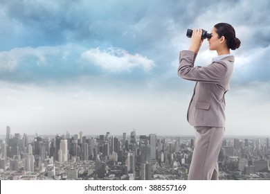 Portrait of a happy businesswoman looking through binoculars against cityscape - Powered by Shutterstock