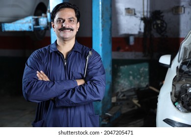 Portrait of a happy car mechanic in moustache standing beside car in service station. Car Specialist is holding car repairing tools. Professional repairman is smiling in modern clean work workshop. - Powered by Shutterstock