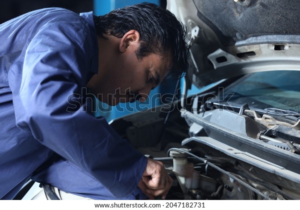 Portrait of a happy car mechanic in\
moustache repairing and examining the car. Car specialist is using\
repairing tools. Repairman wearing a blue mechanic\'s uniform and\
working hard and\
dedicatedly.