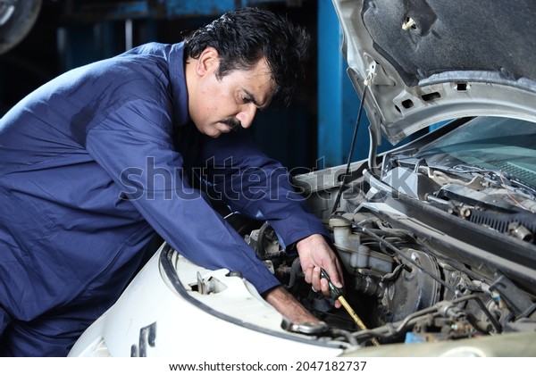 Portrait of a happy car mechanic in\
moustache repairing and examining the car. Car specialist is using\
repairing tools. Repairman wearing a blue mechanic\'s uniform and\
working hard and\
dedicatedly.