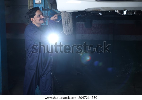Portrait of\
happy car mechanic in moustache repairing and examining the lifted\
car. Car specialist is working on the tyre. Hard working repairman\
wearing mechanic uniform in\
blue.