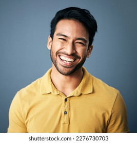 Portrait, happy and carefree with a man in studio on a blue background feeling confident or positive. Face, smile and cheerful with a handsome young male posing on a color wall looking relaxed