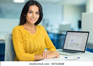 Portrait Of A Happy Casual Businesswoman In Sweater Sitting At Her Workplace In Office