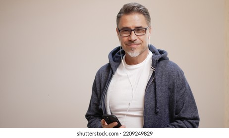 Portrait Of Happy Casual Older Man Smiling, Mid Adult, Mature Age Guy In Glasses, Listening Music On Phone, Isolated On White Background, Copy Space.