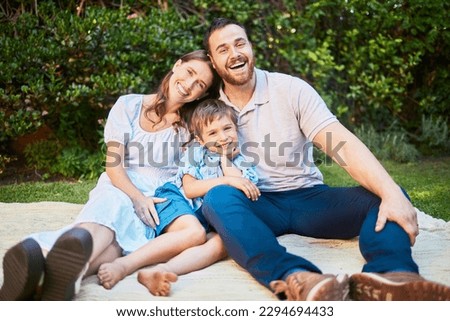 Portrait of a happy caucasian family having a picnic in their garden, sitting on a blanket. Cheerful parents relaxing, enjoying a summer day with their little son. Young family relaxing outside