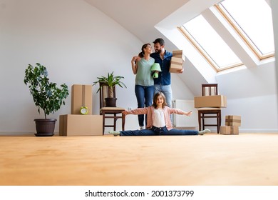 Portrait of happy caucasian family moving in new apartment with flexible little girl doing gymnastics exercise and parents carrying belongings.