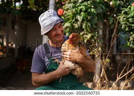 Portrait of happy caucasian farmer holding a brown hen outdoor. Smiling mature man with chicken in hand with copy space.