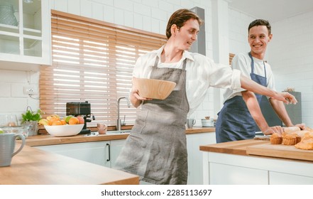 Portrait of the happy caucasian gay couple wearing aprons, looking at each other with smiles and enjoying cooking together in the kitchen at home. LGBT relationships. Gay couple cooking concept. - Powered by Shutterstock