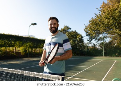 Portrait Of Happy Caucasian Man Playing Tennis Standing By Net On Outdoor Tennis Court. Sport, Healthy Hobbies, Competition, Fitness And Leisure Time Concept.