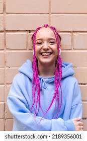 Portrait Of A Happy Caucasian Teenage Hipster Girl With Pink Braids Using An Earphones Against A Pink Brick Wall.Summer And Technology Concept.Generation Z Style.