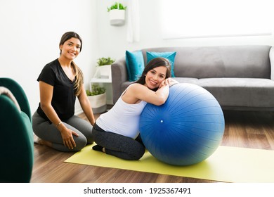 Portrait of a happy caucasian woman and her midwife smiling while sitting in an exercise mat in the living room. Doula using a fitness ball to exercise with an expectant mother