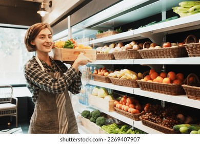 Portrait of happy Caucasian young adult employee holding the basket of fruit with inspiration to work. Saleswoman is setting the grocery store and stocking fruit on the shelves before the store opens. - Powered by Shutterstock