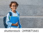 Portrait of happy caucasian young preteen boy elementary middle school pupil in eyeglasses with backpack holding notebook books outside the primary school. Education concept copy space