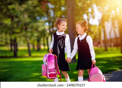 Portrait Of Happy Caucasian Young Smiling Girls Wearing School Backpack Outside The Primary School. Schoolgirl, Elementary School Student Going From School, Graduation, Summer Holidays.