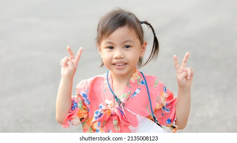 Portrait of happy charming 4 years old cute baby Asian girl, little preschooler child with adorable pigtails braids hair smiling looking to the camera showing 2 fingers doing peace sign.