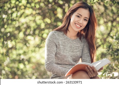 Portrait of happy charming Vietnamese woman reading a book outdoors